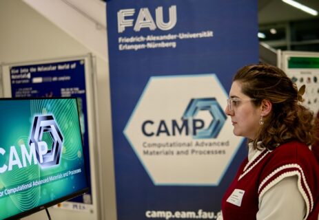 A visitor at the LNDW2025 is looking at the CAMP booth. In the background the CAMP RollUP is visible.